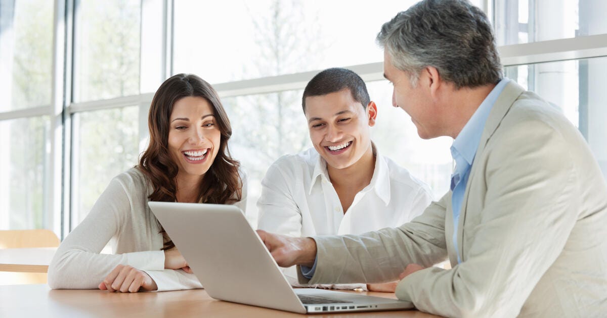 A mature financial consultant advising a happy young couple.