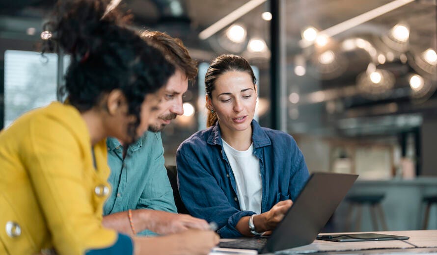 Small group of co-workers working together in a startup business office space. A team of young people in a modern office is discussing their project. Group of business people working. The team are sitting at a board room table looking at a laptop computer