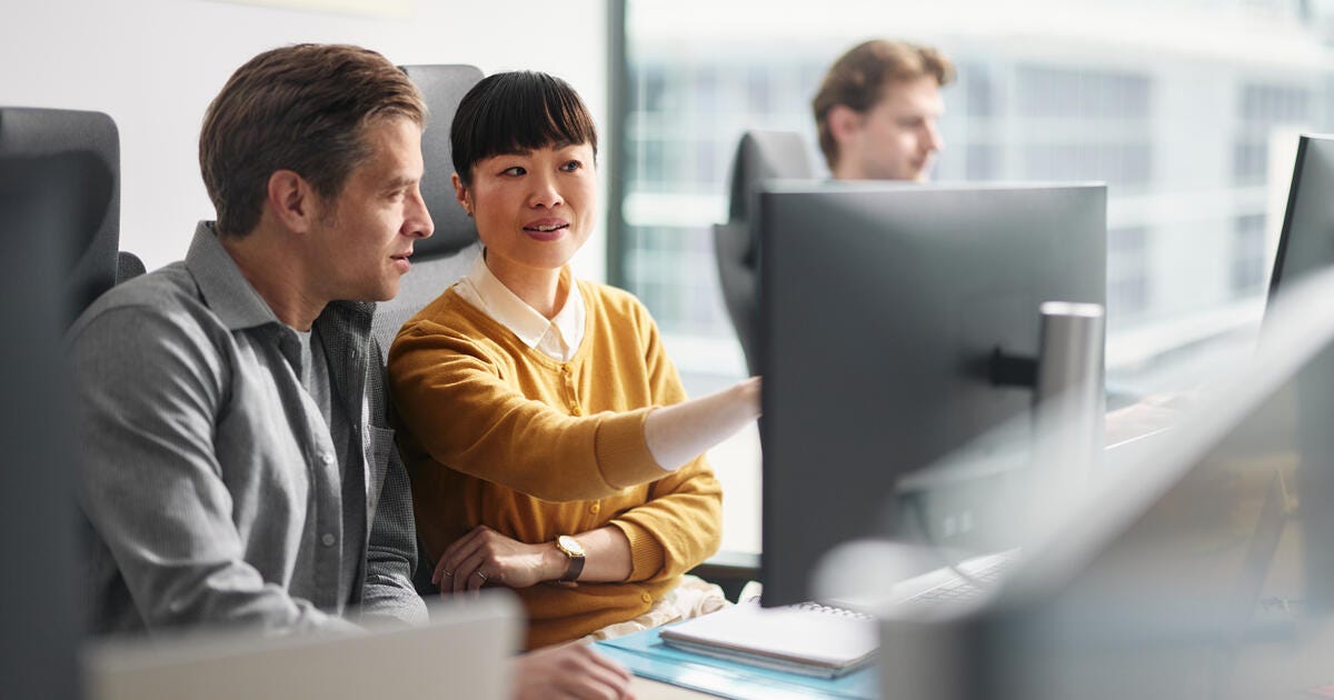 Mid adult programmers cooperating while reading codes on desktop PC at corporate office.