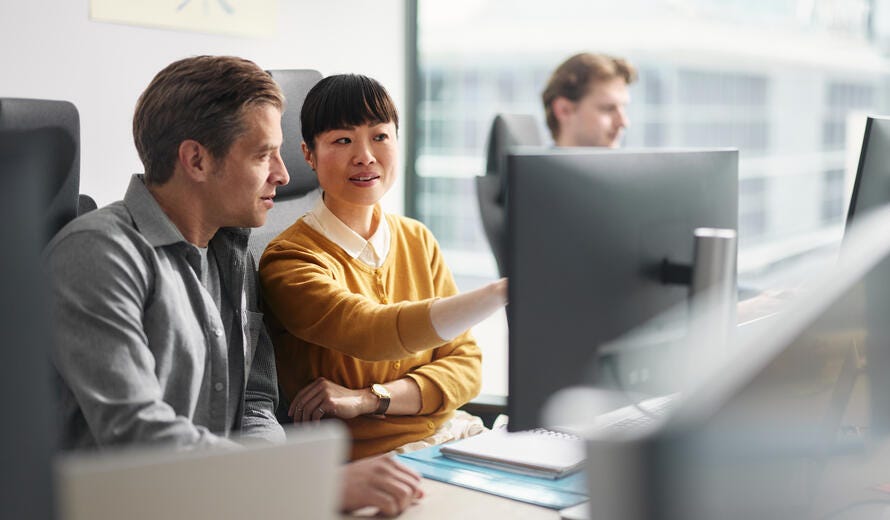 Mid adult programmers cooperating while reading codes on desktop PC at corporate office.