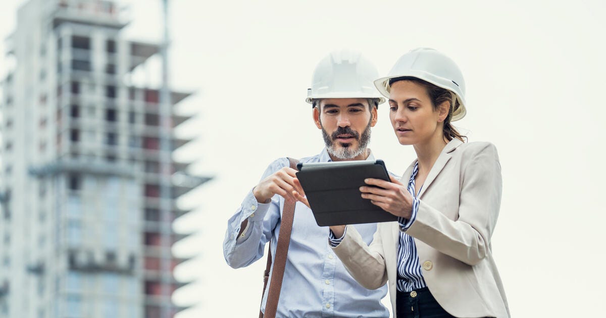 Male and female architects using digital tablet while standing at construction site.